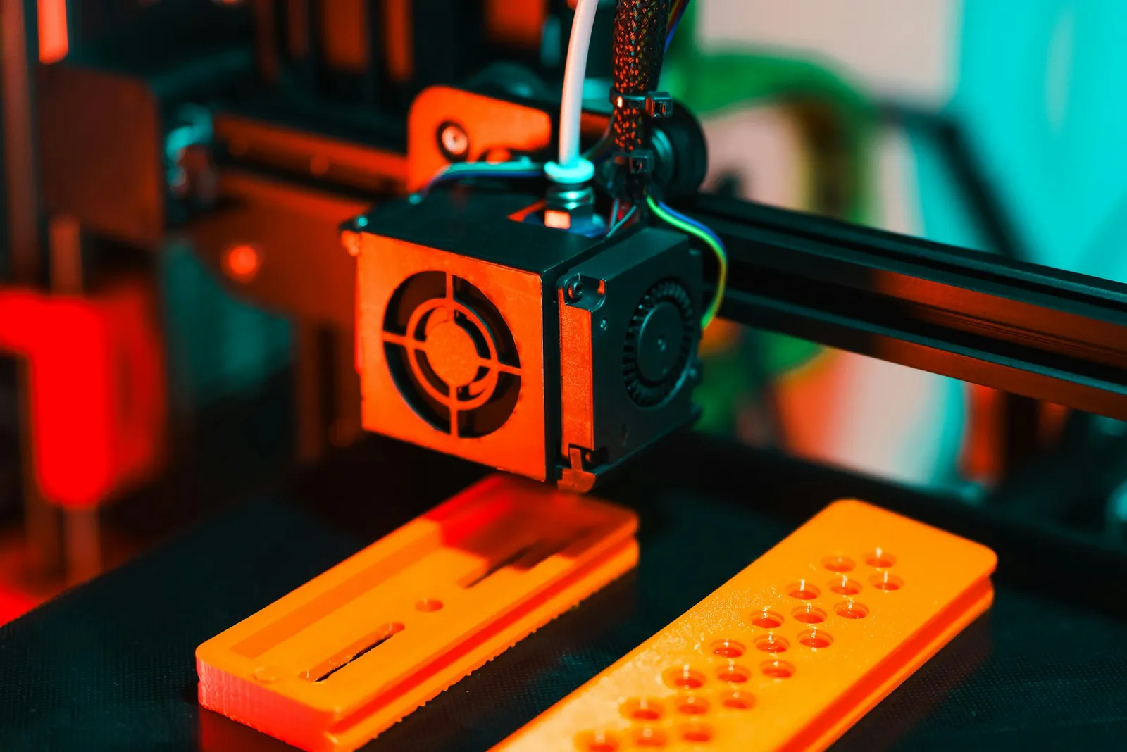 A 3D printer printing orange parts, close-up of the print head