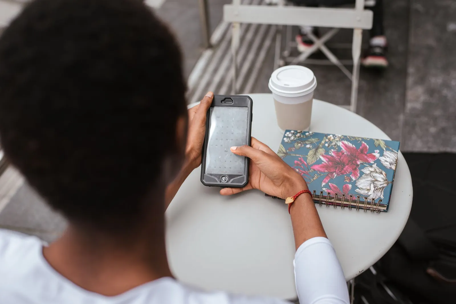 A customer reading her phone at a cafe table with a takeaway cup