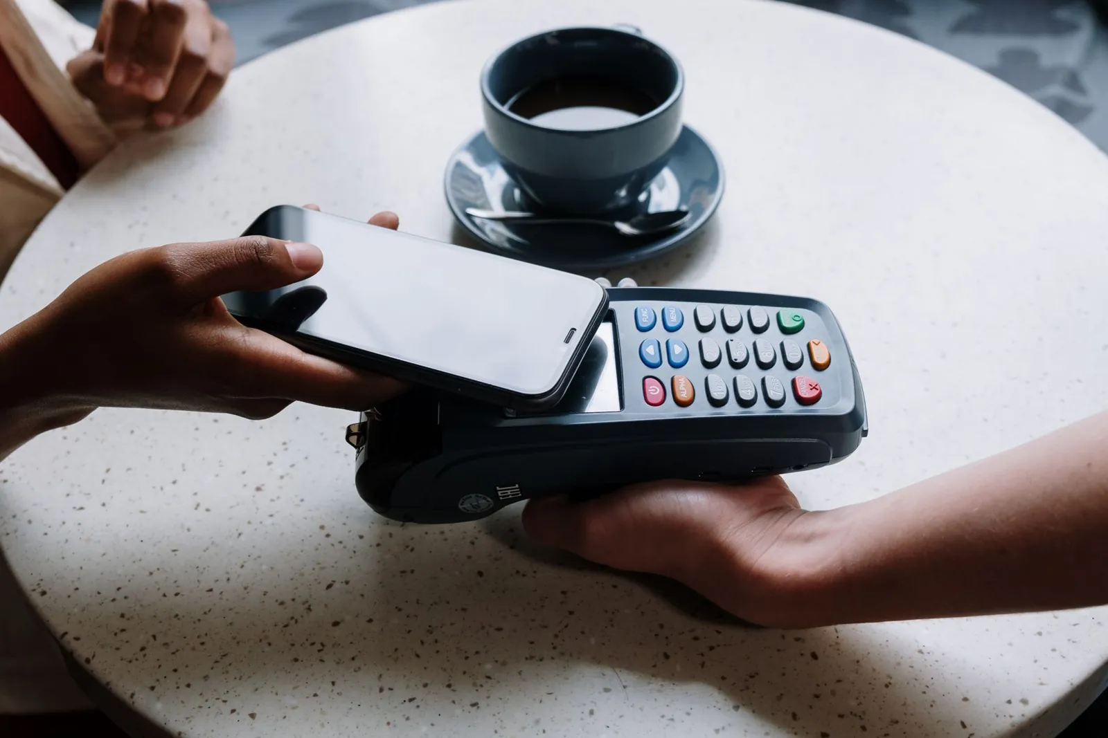 A phone held over a contactless reader on a cafe table