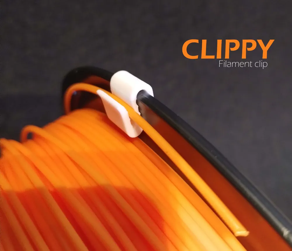White 3D-printed Clippy clip holding the loose end of an orange filament strand against the rim of its spool