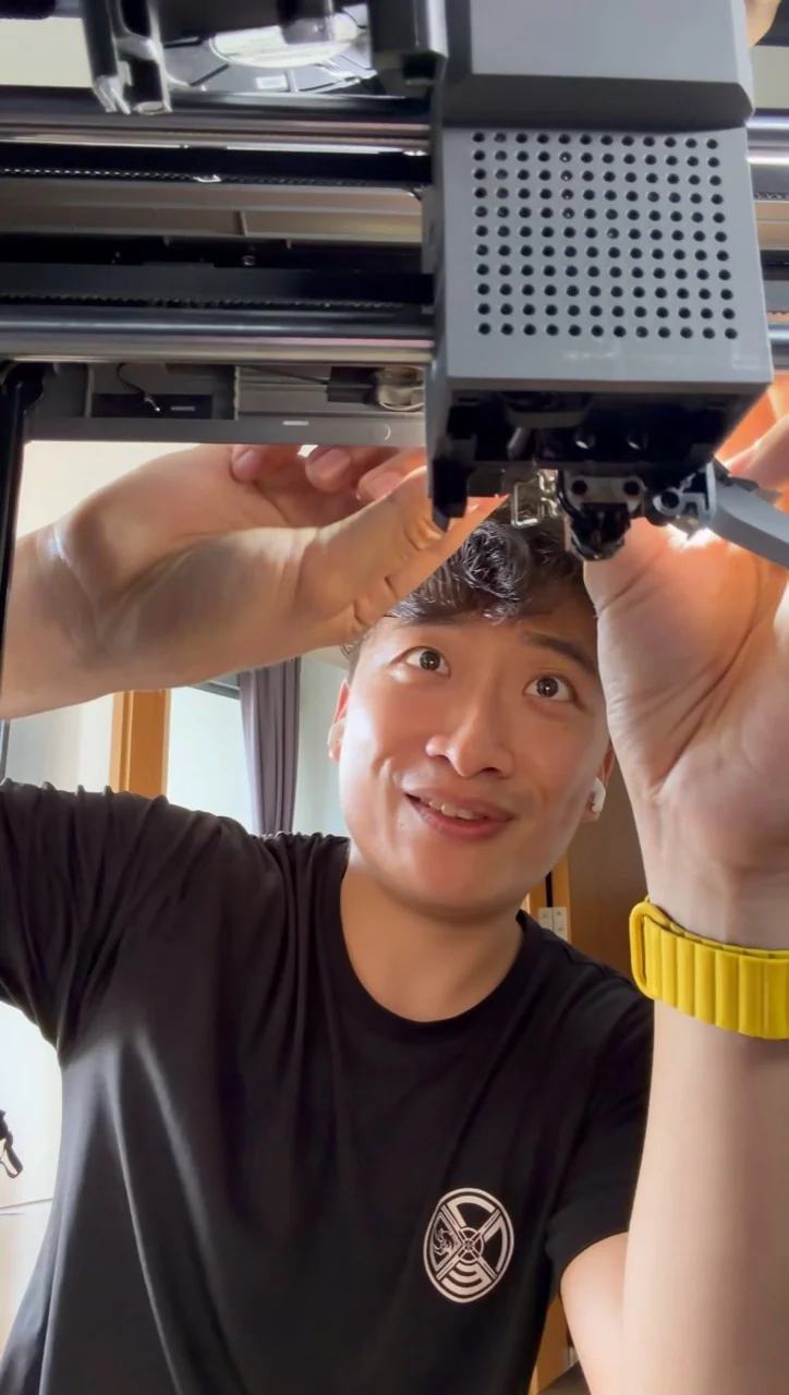 Linhan working on a 3D printer, with his hands around the print head