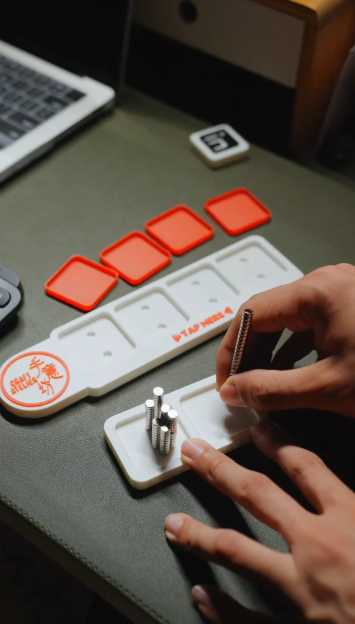 Hands assembling an NFC stand, with colourful printed parts on the workbench